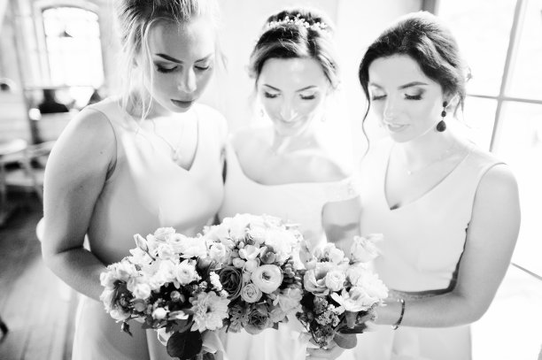 美丽的新娘和可爱的伴娘捧着花束在餐厅里。黑白照片。图片下载