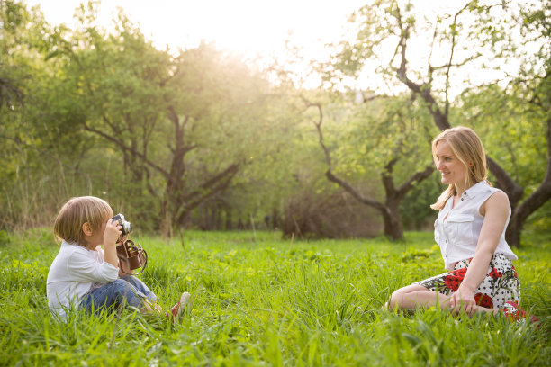 特写的可爱的小男孩和他美丽的年轻的母亲与复古相机拍照。快乐的家庭在夏天的公园拍摄照片。在户外。图片下载