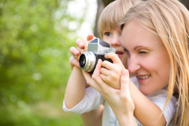 特写的可爱的小男孩和他美丽的年轻的母亲与复古相机拍照。快乐的家庭在夏天的公园拍摄照片。在户外。图片下载