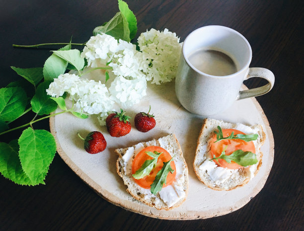 早餐有烤面包(西红柿，奶油奶酪，rucola)，一杯卡布奇诺，新鲜草莓和装饰绣球花。图片下载