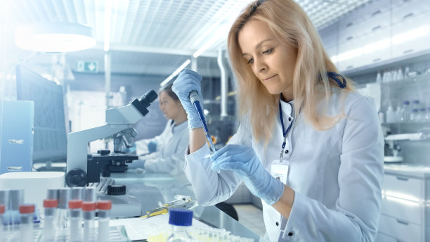 女研究科学家使用微量移液器在大现代实验室中填充试管。背景科学家们正在工作素材图片