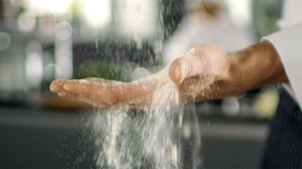 著名餐厅的面包师在现代化的厨房里用手筛面粉。图片下载