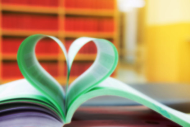 心形的纸放在图书馆的桌子上，以书架上的红色书籍为背景，效果模糊图片下载