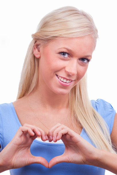 年轻的金发女人在蓝色衬衫显示心形符号在白色的背景图片下载