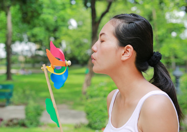 年轻的女性在花园里吹风力涡轮机。图片下载