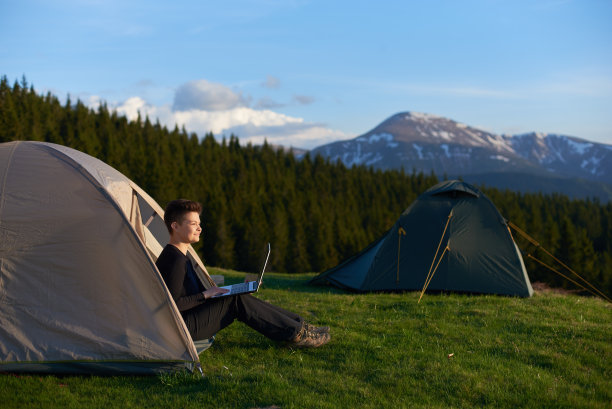 快乐的女孩在山里享受日出坐在她的帐篷里，在笔记本电脑上工作，露营视频网站旅行移动技术互联网在线学习旅游。图片下载