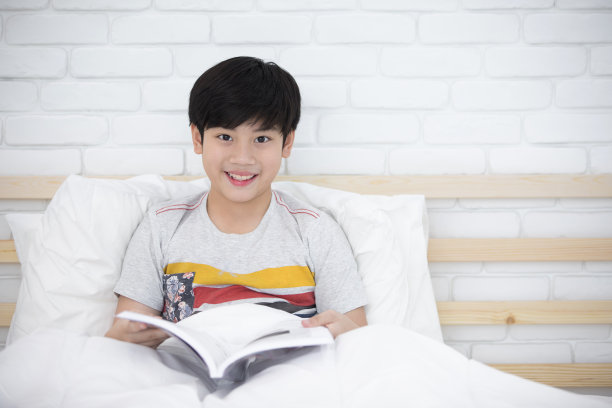 亚洲男孩休息在床上看书在家。图片下载