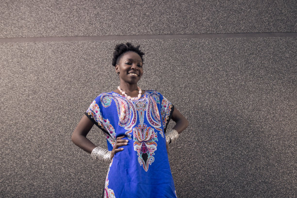 一个，年轻的成年人，非洲裔美国人，女性，20-29岁，看着镜头，在户外灰色的墙壁，穿着蓝色的衣服，微笑着，手放在臀部图片下载