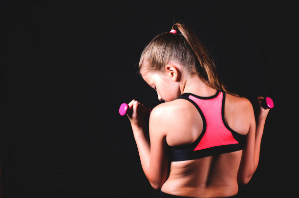 年轻的健身女孩在黑色背景下举着哑铃。运动或健康的生活方式概念图片下载