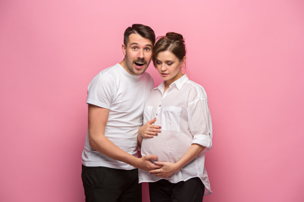 英俊的男人听着他美丽的怀孕妻子的肚子微笑着图片下载