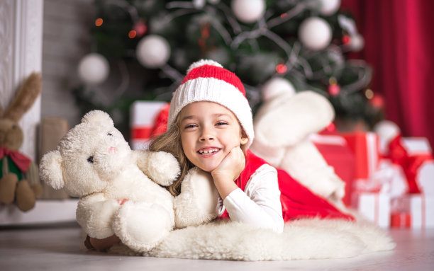 可爱的小女孩在圣诞树旁的地板上抱着一只小熊，在摄影棚拍摄。图片下载