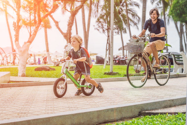 快乐的家庭在户外骑自行车，微笑。爸爸骑自行车，儿子骑平衡自行车图片下载