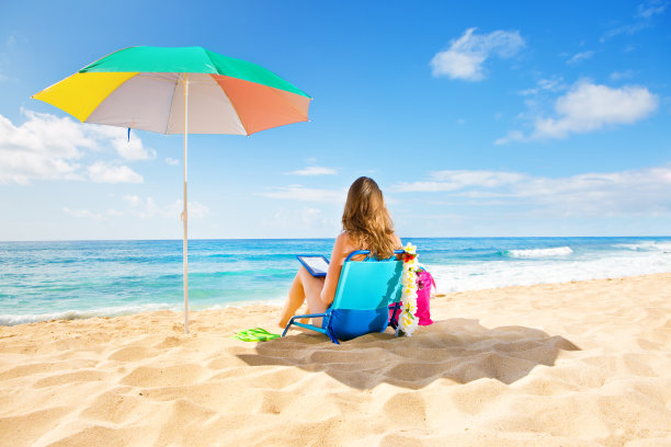 在夏威夷海滩上用平板电脑阅读的女人图片下载