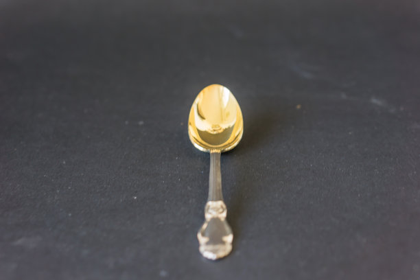 特写银咖啡勺与镀金的一块在黑色的背景。饰品上的提手，怀旧的概念。聚焦深度浅。图片下载