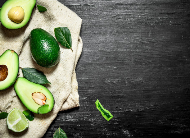 鳄梨，酸橙和树叶。以黑色木制为背景。图片下载