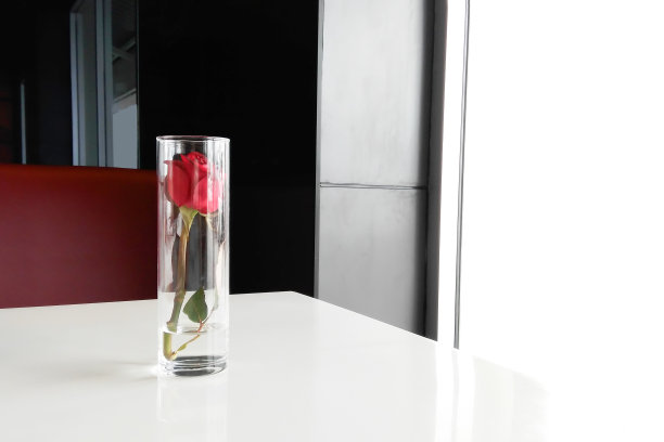 桌上放着一只玻璃杯里的红玫瑰。爱的概念。通过智能手机。图片下载