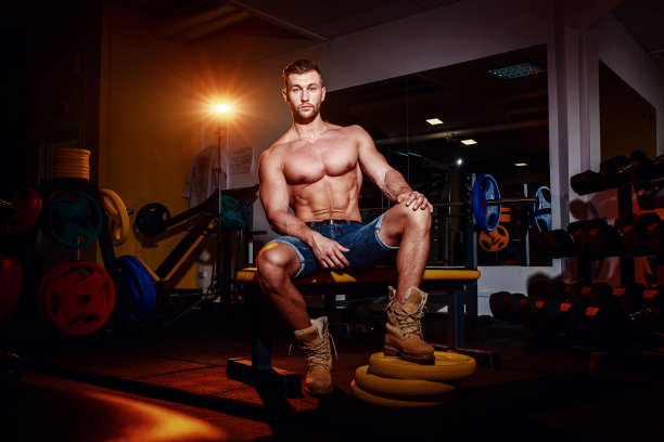 健美运动员坐在举重台上休息。一个肌肉发达的男人在健身房里对着镜头微笑。图片下载