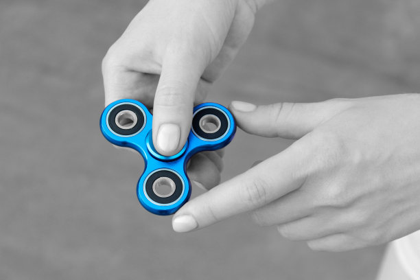 女孩手拿蓝色金属转轮在街上玩，女性的手拿着流行的指尖转轮玩具在灰色的背景，黑白，黑白照片图片下载