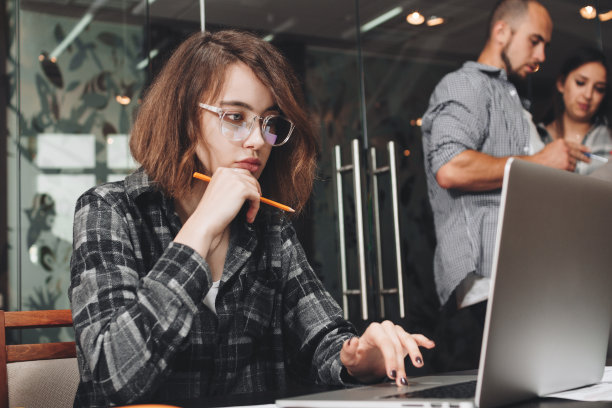 沉思的商务女性戴着眼镜在笔记本电脑上工作的照片。商业团队的合作伙伴在阁楼办公室。美丽的女孩拿着铅笔，思考着新的创业图片下载