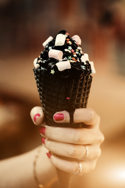 趋势锥形的木炭冰淇淋与糖果和食品粉，粉红色和蓝色蓬松的甜蜜在妇女的手臂。模糊的散景城市背景，阳光耀斑文字和设计素材图片