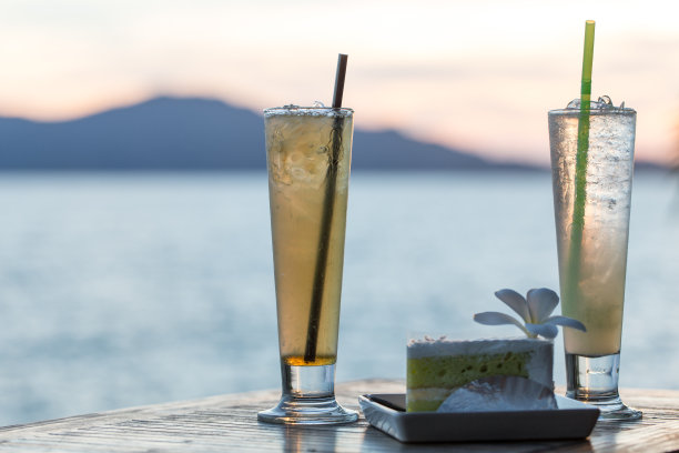 木桌上的冰柠檬茶和日落时的海滩景色。图片下载