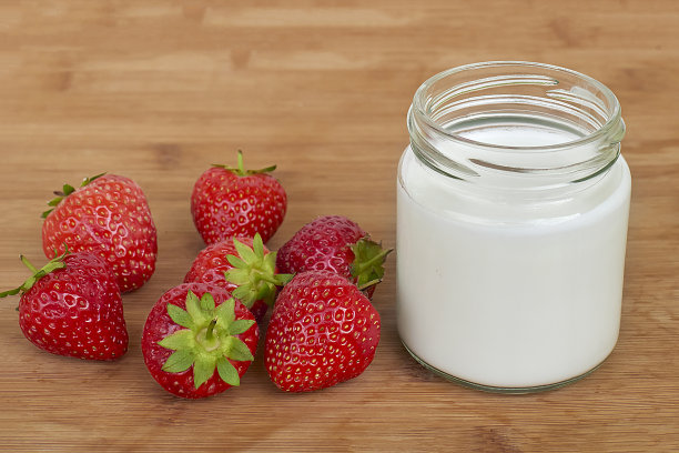 玻璃罐与酸奶和七个草莓在一个木制背景水平近距离图片下载