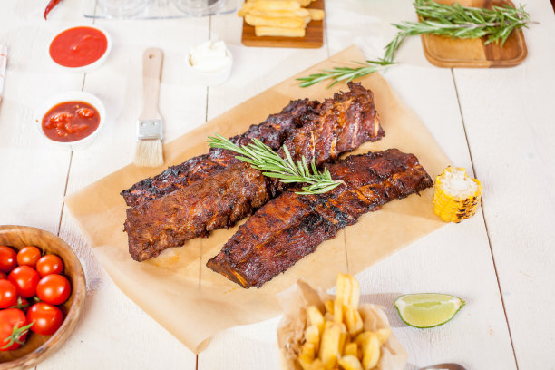 夏季烧烤的辣烤排骨配上薯条、玉米和新鲜番茄，放在旧的木砧板上图片下载