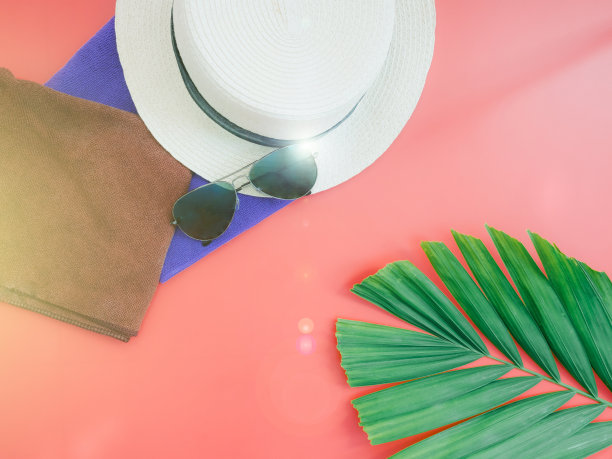 平躺夏天概念与沙滩帽和蓝色和棕色织物在红色背景与绿色热带棕榈叶装饰图片下载