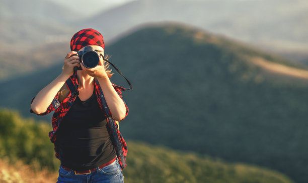 夏日日落时分，一名女旅游摄影师带着相机在山顶徒步旅行图片下载