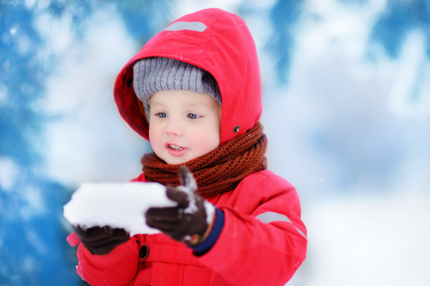 穿着红色冬装的小男孩玩冰块的肖像图片下载