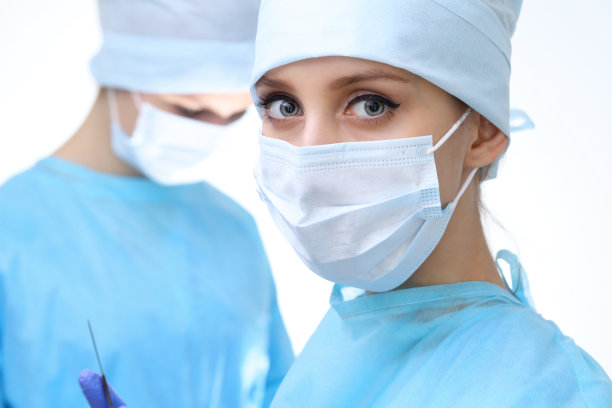 近距离的外科医生妇女看着摄像机，而同事在手术室的背景，孤立图片下载