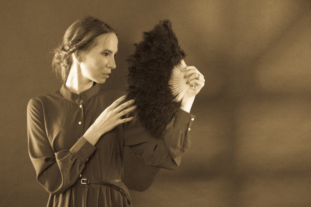 女性复古风格手持羽毛扇，深褐色调图片下载