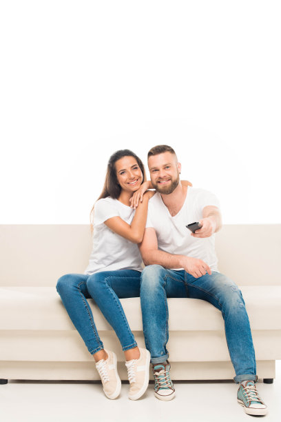 “这是一对年轻迷人的夫妇用遥控器看电视的照片，孤立在白色屏幕上。图片下载