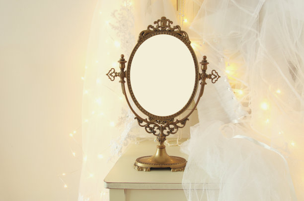 古老的椭圆形镜子和美丽的白色婚纱和椅子上的面纱与黄金花环灯图片下载