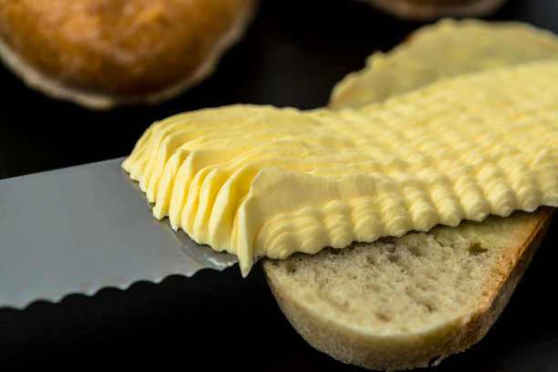 黄油与美丽的污点和刀上的一片面包在一个黑暗的背景特写图片下载