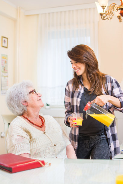 孙女给奶奶倒新鲜橙汁。家庭护理的概念。图片下载