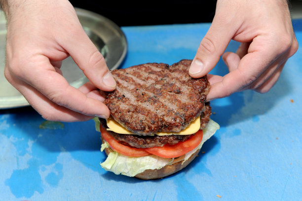 厨师在准备好的汉堡面包上添加汉堡。在厨房里准备和做汉堡包。图片下载
