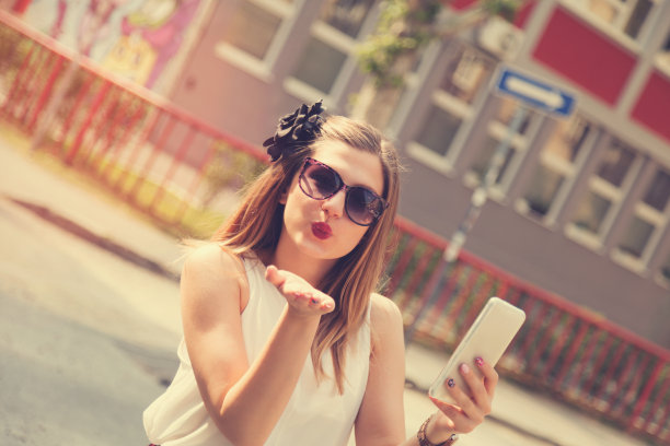 可爱的女孩在街上用手机时送了一个飞吻。图片下载