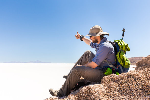 旅游背包客坐在山顶，上面的盐沙漠，玻利维亚。图片下载