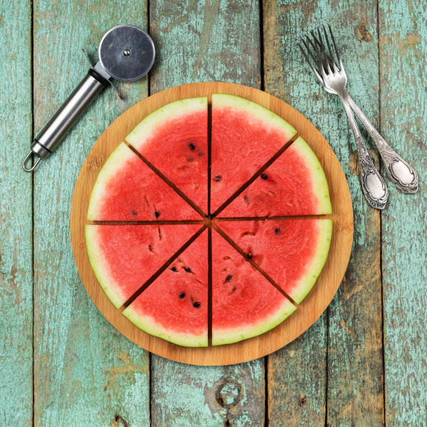 新鲜多汁的西瓜，切得像披萨，用叉子和披萨刀食用。健康的素食小吃图片下载