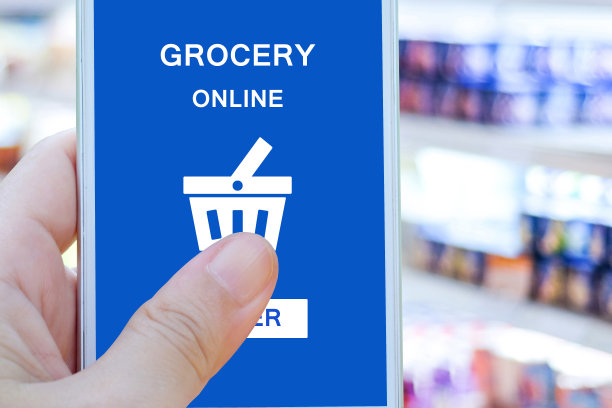 手持智能手机与杂货网上购物屏幕上模糊超市背景，零售业务和技术概念图片下载