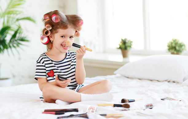 漂亮有趣的小女孩在化妆，在床上笑图片下载