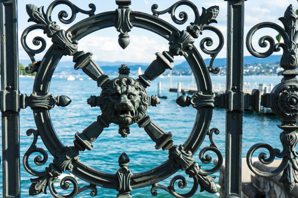 湖水透过铁栅栏看到，铁栅栏上有一个狮子头的历史装饰图片下载