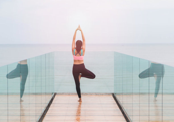 早晨，亚洲妇女在海边的一个木制甲板上练瑜伽。反射在镜子里。图片下载