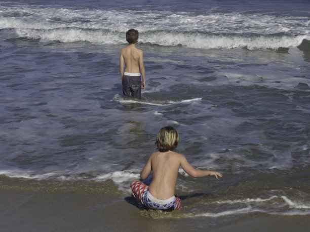 两个男孩在海滩上玩海浪。锡拉丘兹,西西里岛。图片下载