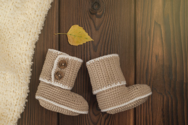 手工钩针婴儿靴子和秋天的多色树叶在木制的背景，色调的照片图片下载