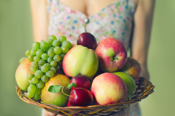 一个年轻女子手里拿着一个大木盘，上面盛着成熟的水果。收获的概念图片下载