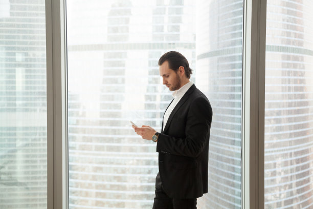 严肃的商人在现代办公室靠窗看手机图片下载