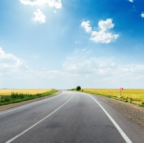 田野里的柏油路和湛蓝的天空，乌云和阳光图片下载