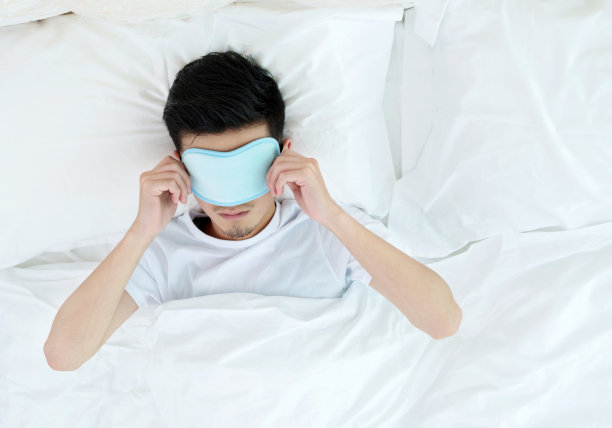 在床上戴着睡眠面罩的年轻人图片下载